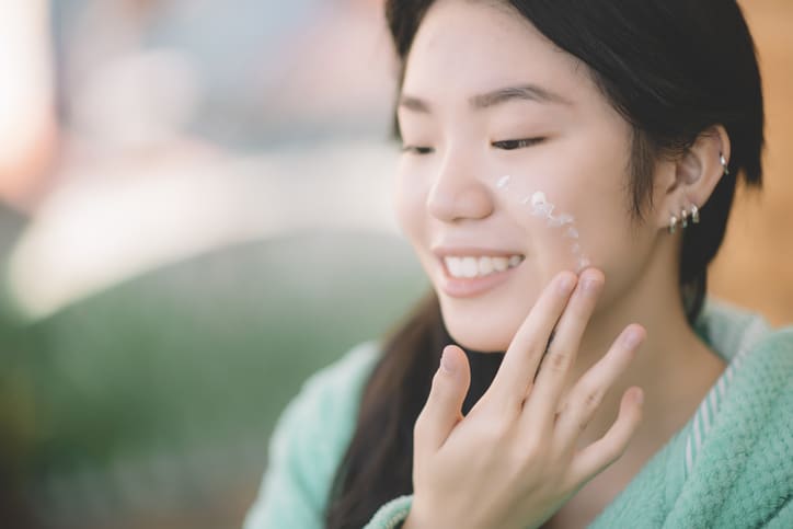 a teenage girl of Chinese heritage is seen applying moisturiser facial cream on hand and face