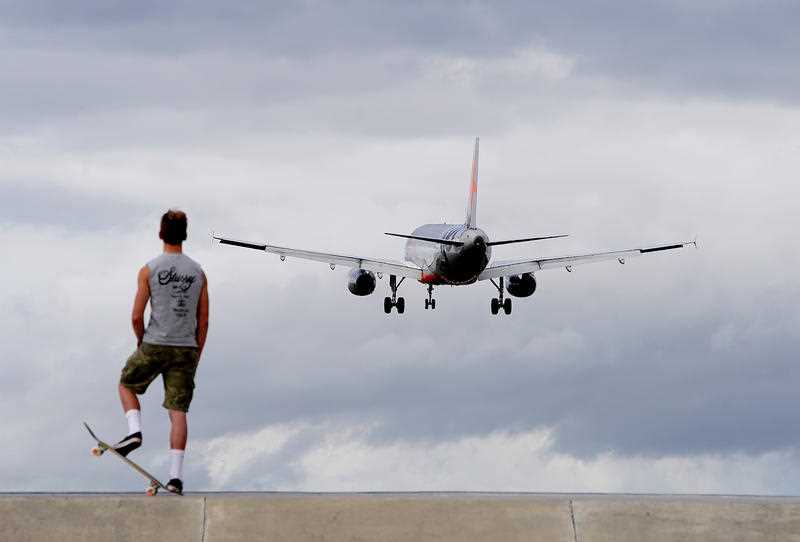 A JetStar plane is seen taking off as a skateboarder watches on from a distance