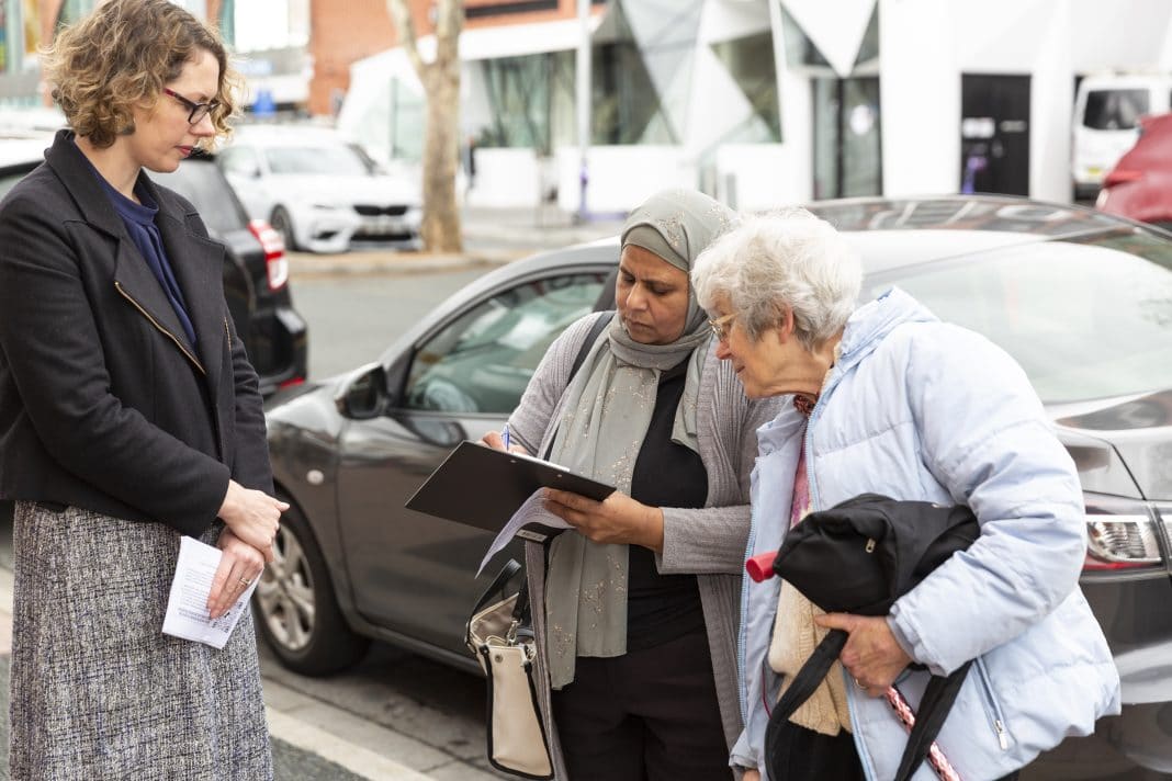 Alicia Payne MP looks on as 2 mature female constituents sign a petition outside Braddon Centrelink office