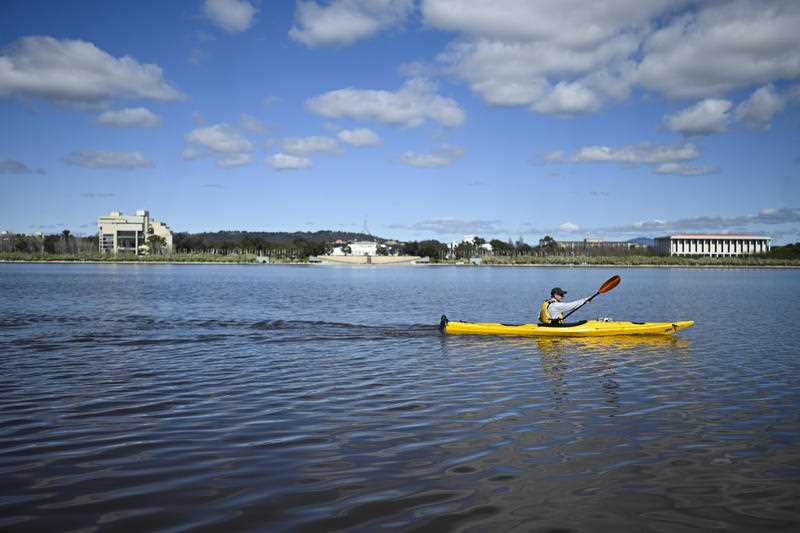 A person paddles a yellow kayak on Lake Burley Griffin in Canberra on a sunny day