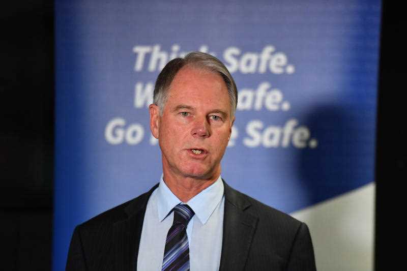 middle aged man in suit speaking in front of a 'Think Safe. Work Safe. Go Home Safe' sign