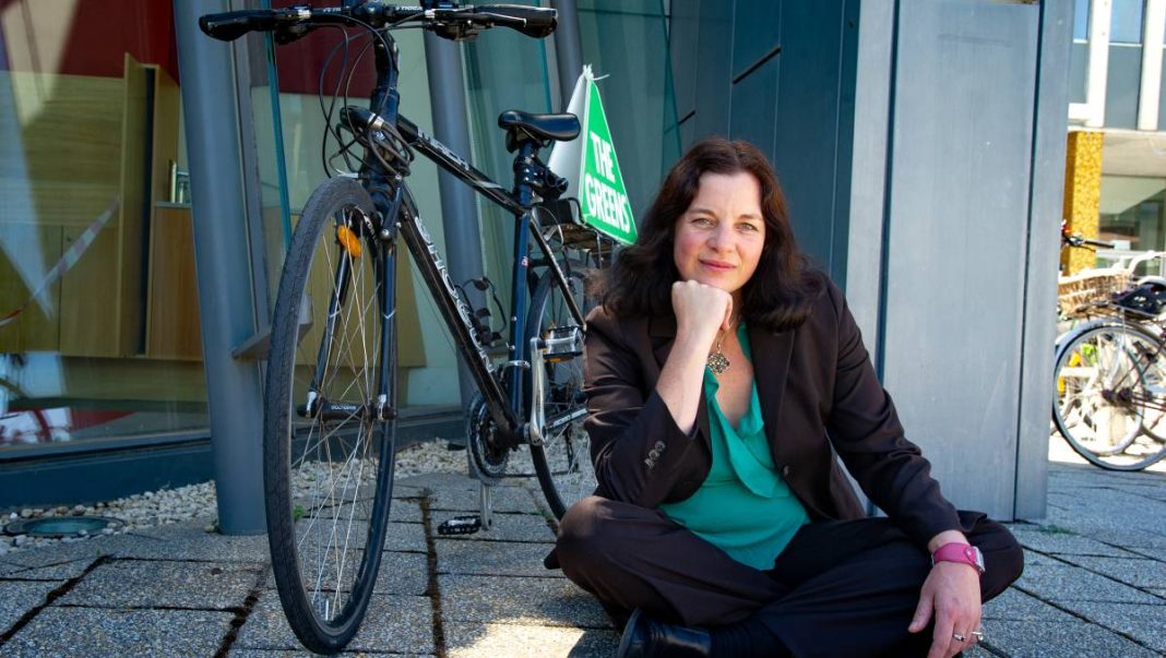 ACT Greens MLA Ms Jo Clay sitting on the ground beside a bicycle