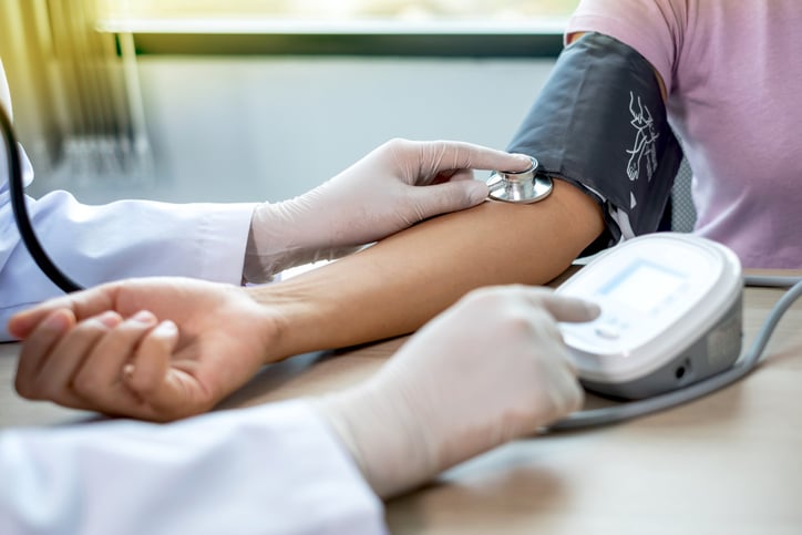 Doctor evaluates the patient with a stethoscope, blood pressure monitor and records the results.