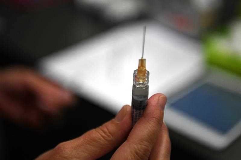 A hand is seen holding a flu immunisation needle