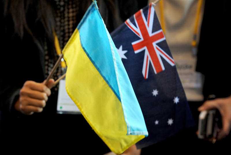 a hand is seen holding a small Ukrainian flag and Australian flag