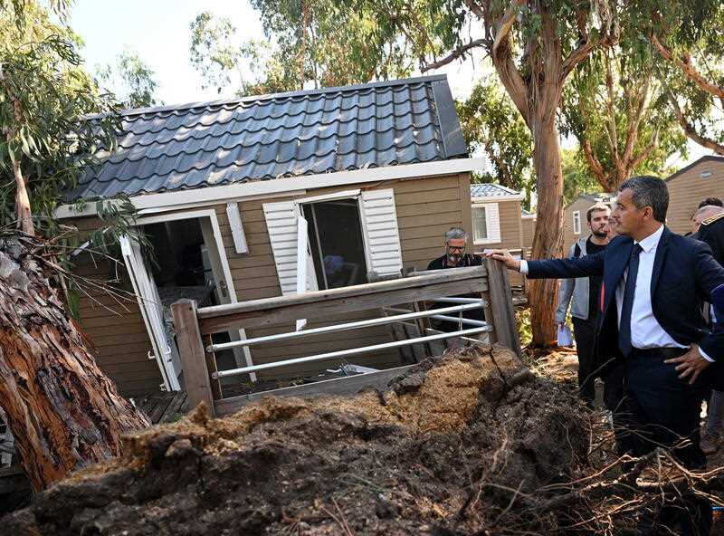 France's Interior Minister Gerald Darmanin (R) stands next to a damaged bungalow at La Pinede camping site in Calvi, Corsica, France, 19 August 2022.
