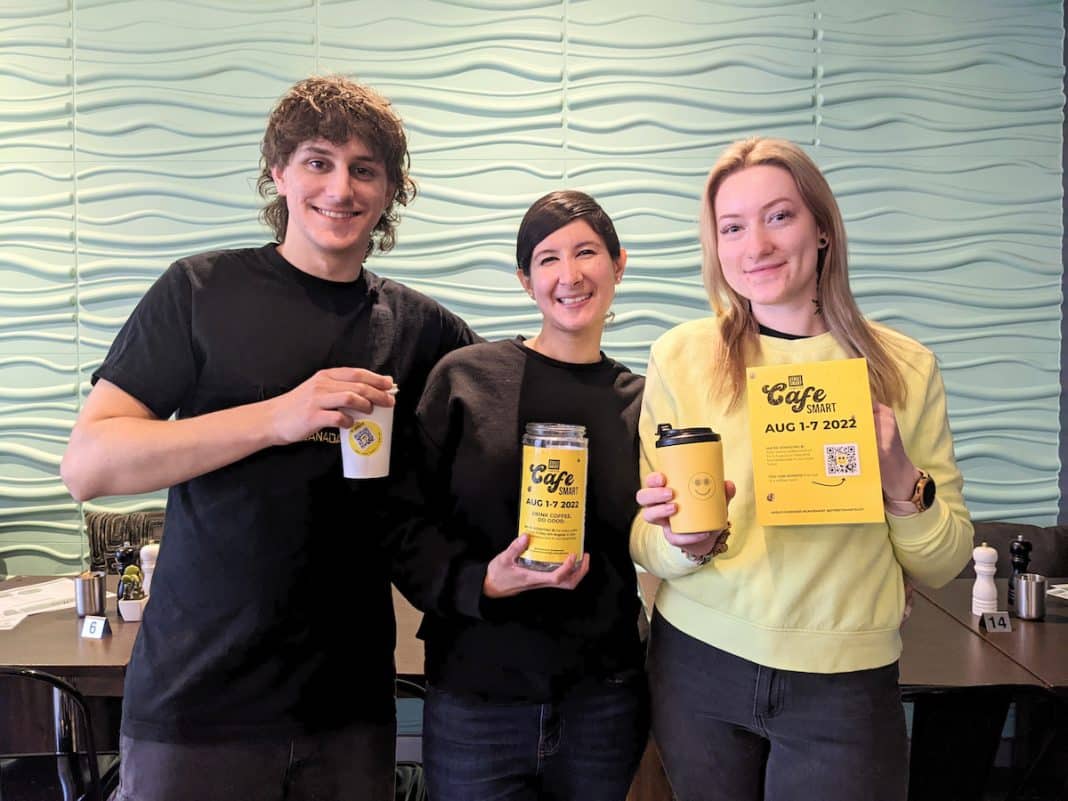 three people in a cafe holding yellow CafeSmart signage