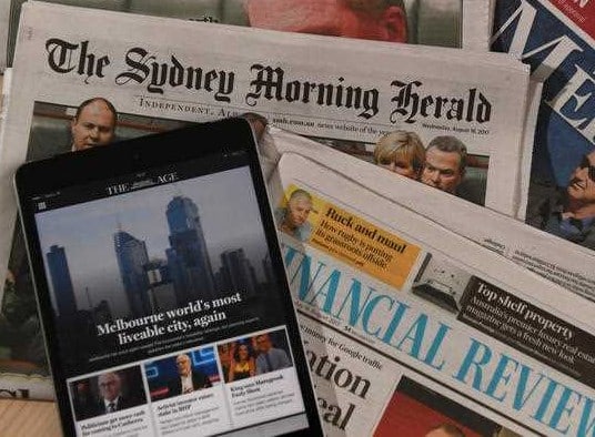 The Age is seen on a tablet screen resting on copies of The Sydney Morning Herald and Financial Review newspapers