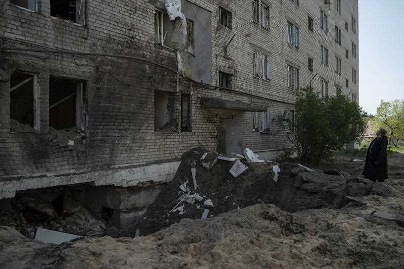 A woman stands next to a crater from an explosion that damaged an apartment and a basement of a residential building in Ukraine