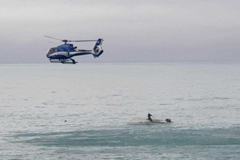 A helicopter flies overs an upturned boat with a survivor sitting on the hull off the coast of Kaikoura, New Zealand, Saturday, Sept. 10, 2022.