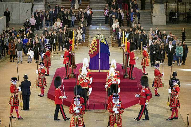 The guard is changed while members of the public file past the coffin of Queen Elizabeth II, draped in the Royal Standard with the Imperial State Crown and the Sovereign's orb and sceptre, lying in state on the catafalque in Westminster Hall, at the Palace of Westminster, in London