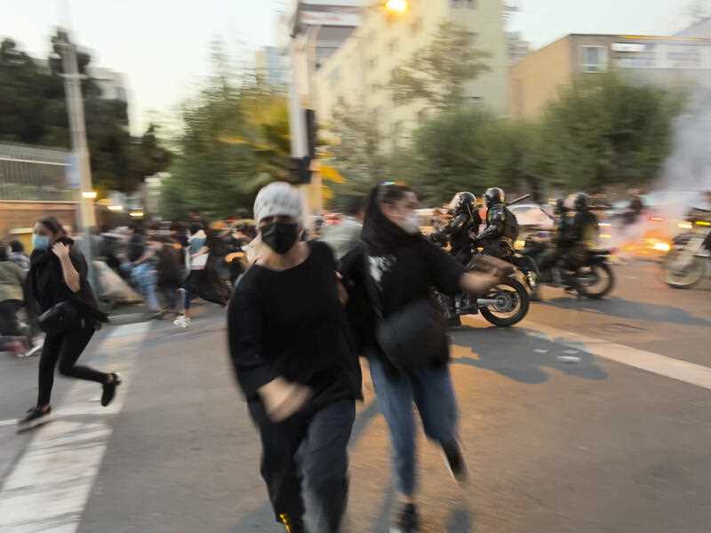 women run away from anti-riot police during a protest of the death of a young woman who had been detained for violating the country's conservative dress code, in downtown Tehran, Iran.