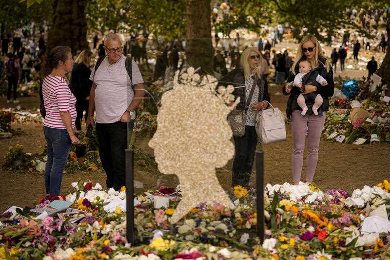 People bring floral tributes to Queen Elizabeth II, the day after her funeral in London's Green Park, Tuesday, Sept. 20, 2022