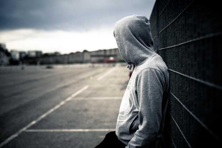 Lonely male wearing hoodie is seen in a desolate urban environment