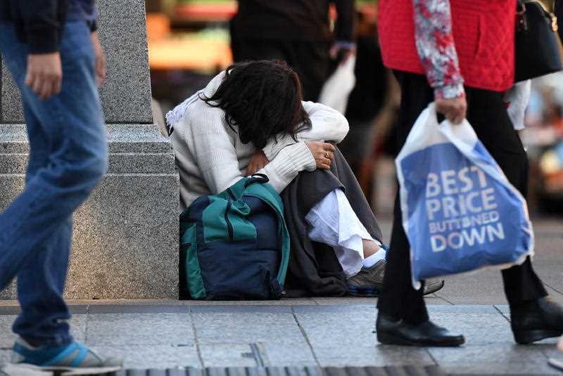 A young homeless woman sits on a street corner in central Brisbane