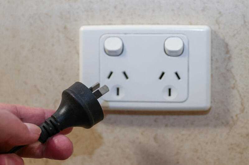 A hand is seen plugging an electric appliance cord into a power point