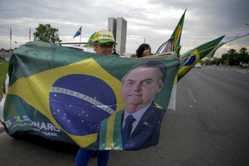 A woman holds a Brazilian flag with the image of Brazilian President Jair Bolsonaro, who is running for another term, after general election polls closed in Brasilia, Brazil, Sunday, Oct. 2, 2022