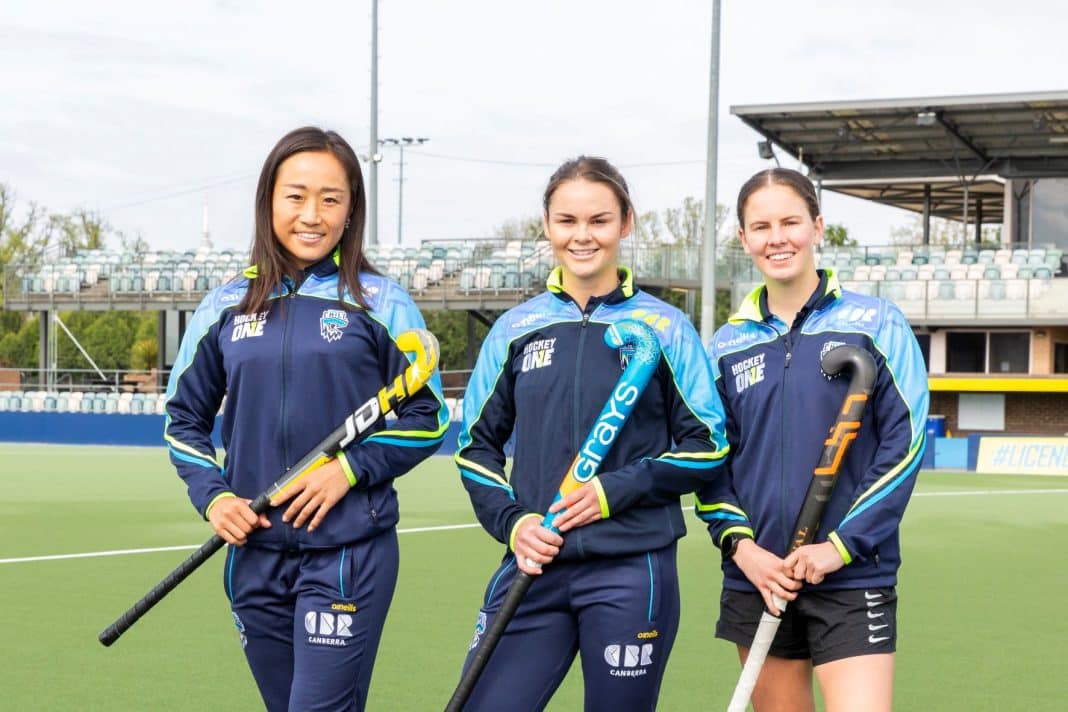 3 female hockey players with sticks standing on the pitch