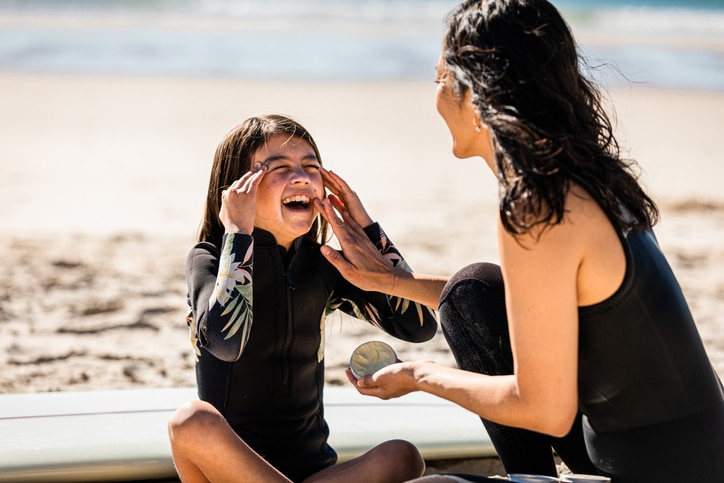 Aussie mums helps her young daughter apply sunscreen at the beach