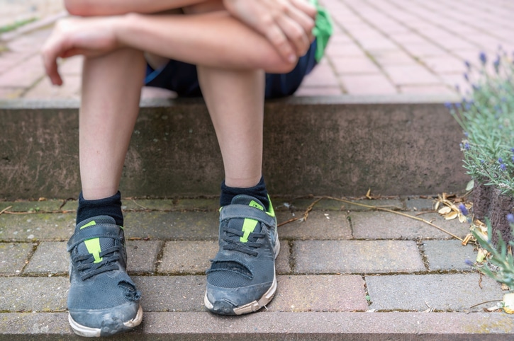 Young boy wearing worn out shoes