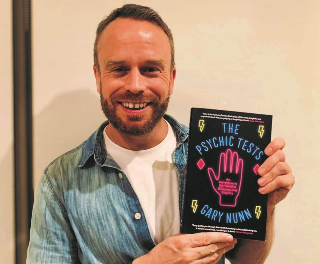 smiling male author with a copy of his book, The Psychic Tests