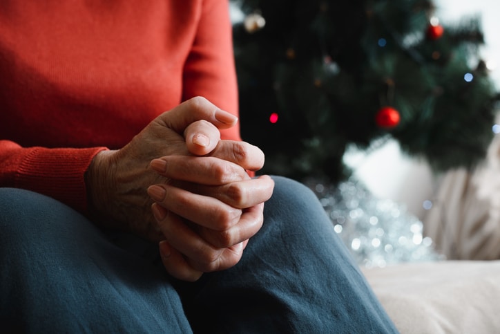 Close-up of an elderly woman's hand against background of decorated Christmas tree.