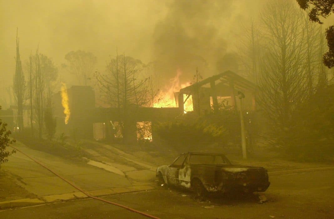 A burnt out car in the driveway as a house in the Canberra suburb of Torrens goes up in flames on 18 January 2003