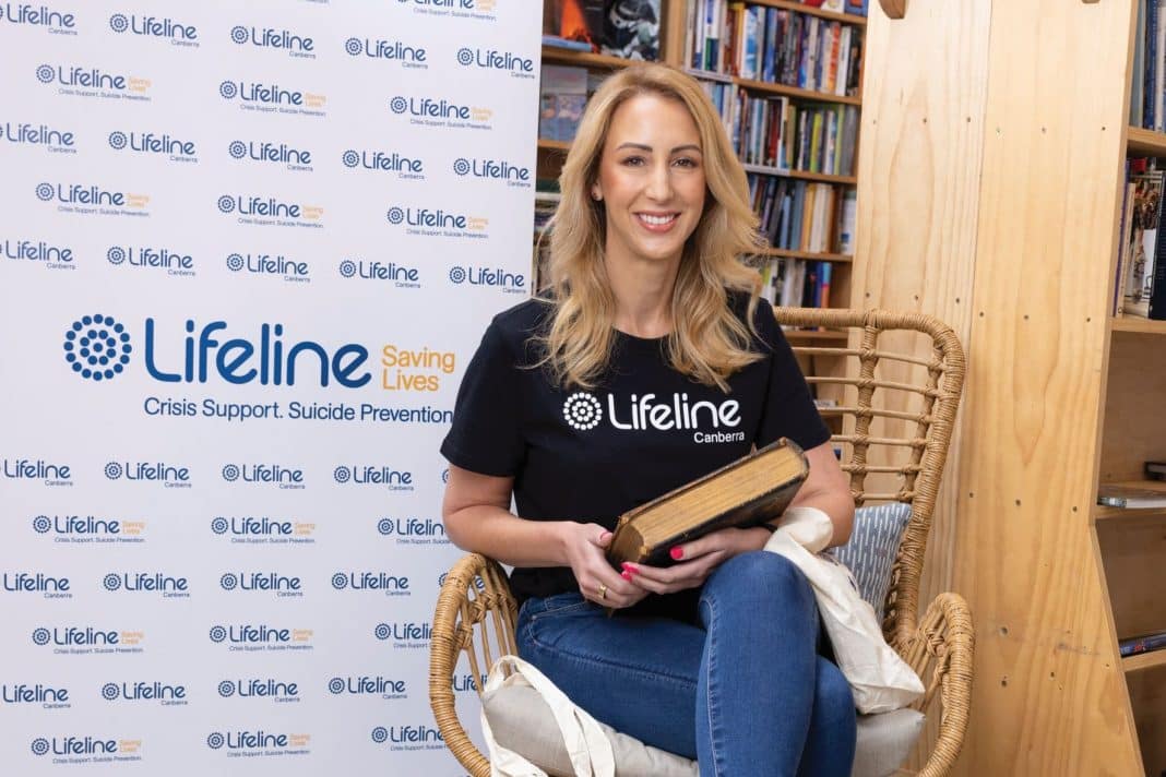 Lilfeline Canberra CEO Carrie-Ann Leeson sitting in a chair with a rare, collectible book at the charity's Book Lovers Lane bookstore.