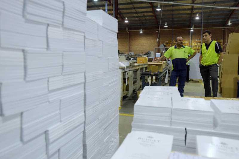 2 men in hi-viz look at stacks of reams of white paper