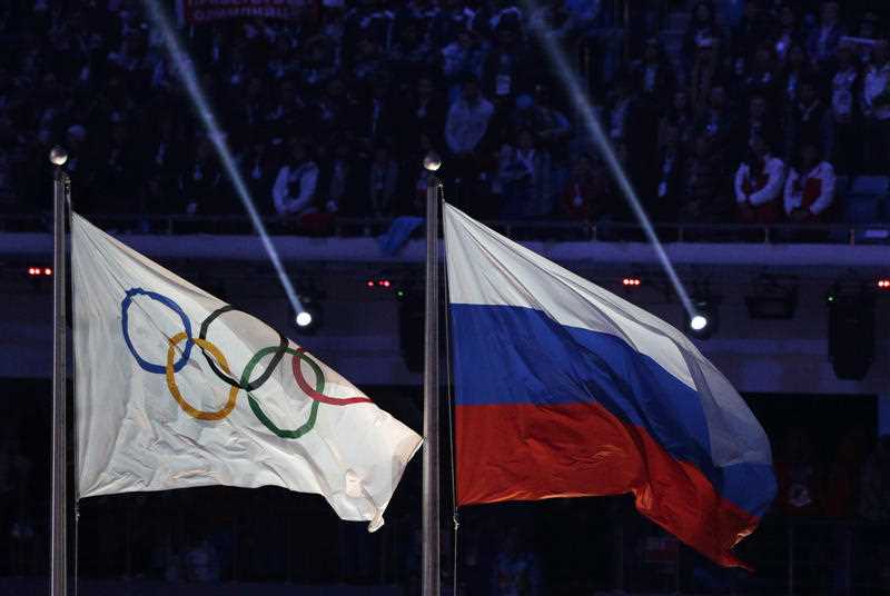 the Russian national flag, right, flies after next to the Olympic flag during the closing ceremony of the 2014 Winter Olympics in Sochi, Russia