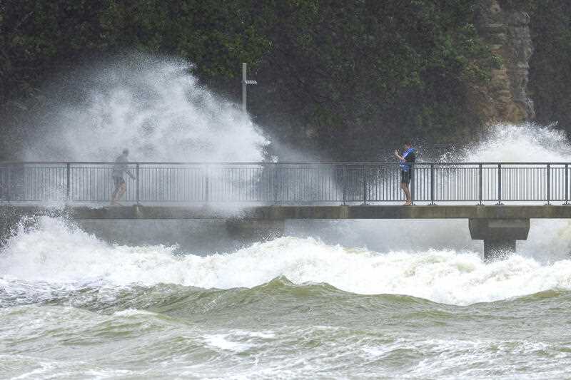 People watch as waves crash against the cliffs at an Auckland beach as a cyclone hits the upper parts of New Zealand, Sunday, Feb. 12, 2023