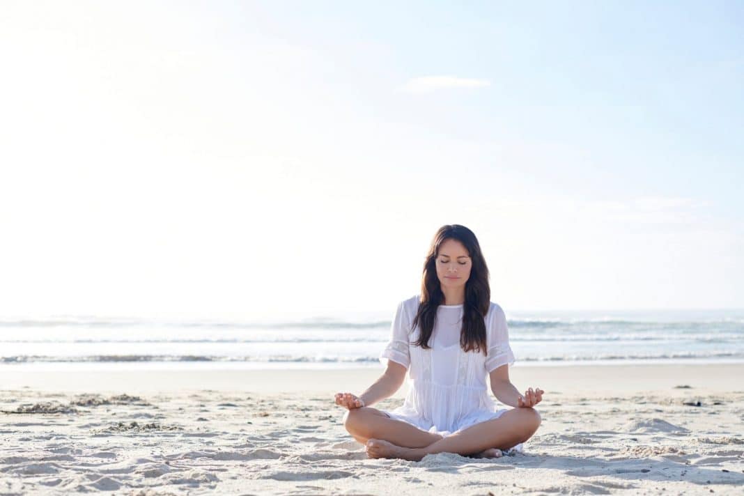 serene brunette in white dress meditating on the beach