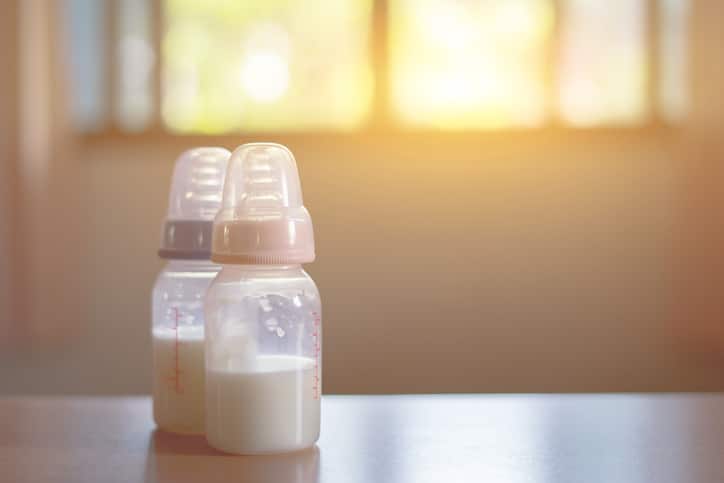 2 baby bottles containing milk are seen on a kitchen bench