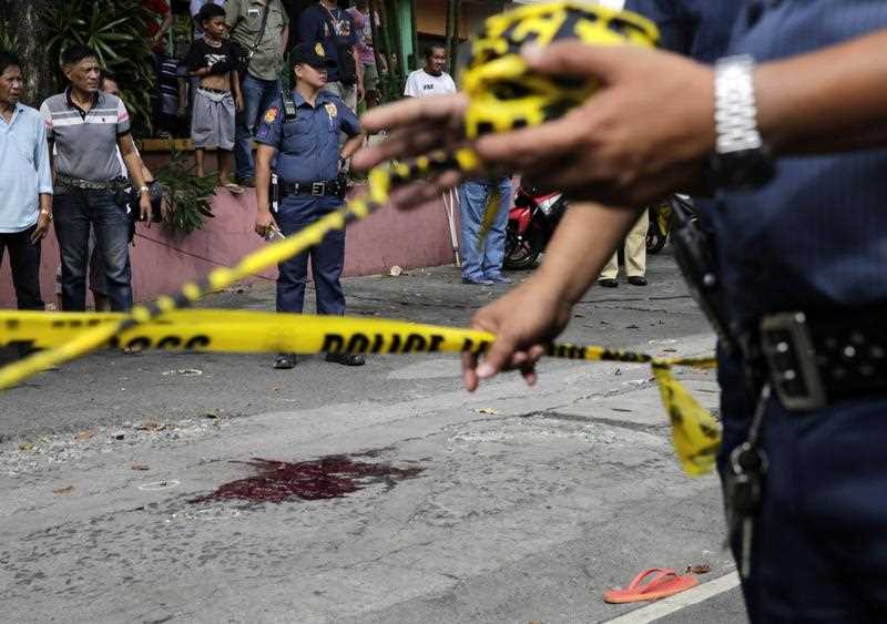 Filipino policemen install police line at the scene of a crime after a victim was shot