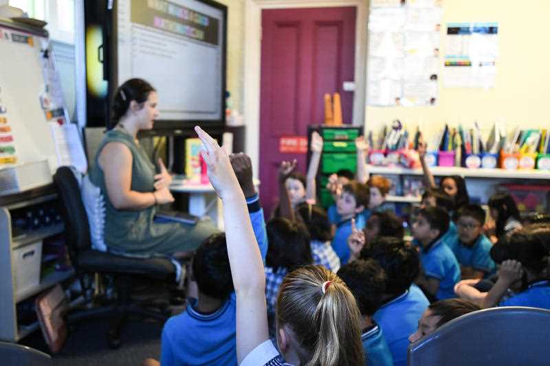 A female teacher and group of young students are seen in a classroom