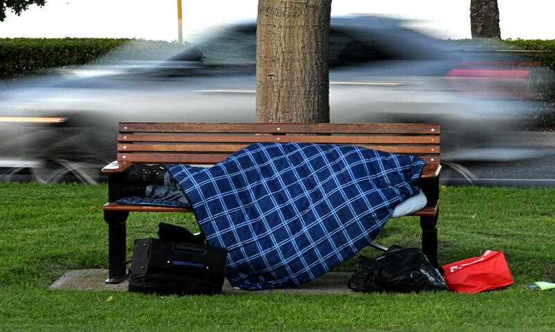 A homeless person is seen sleeping on a park bench