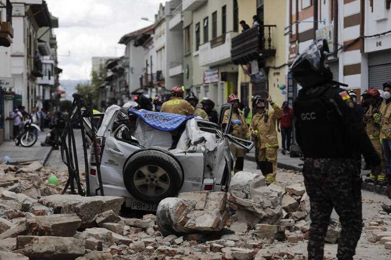 A police officer looks up next to a car crushed by debris after an earthquake shook Cuenca, Ecuador, Saturday, March 18, 2023