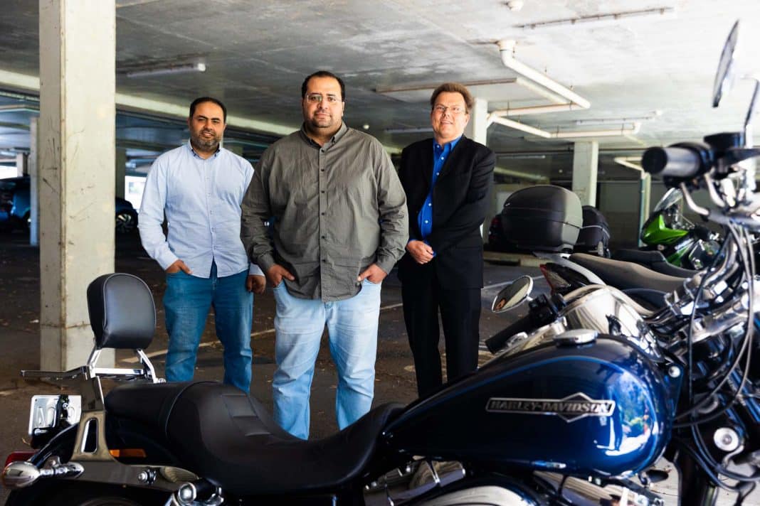 3 male university researchers standing near motorbikes