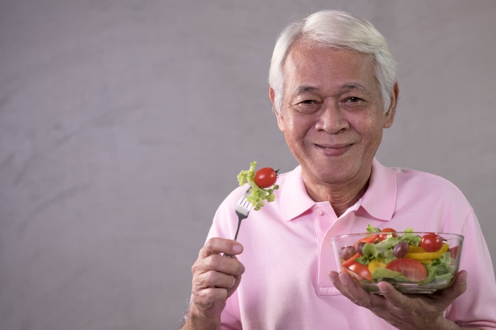 Asian senior man in joyful postures with hand holding salad bowl
