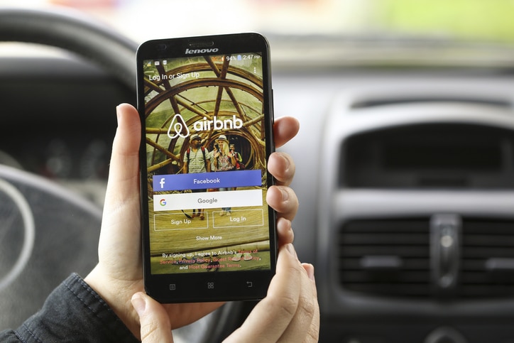 Close-up of an unrecognizable woman using the Airbnb App on a smartphone in a car.