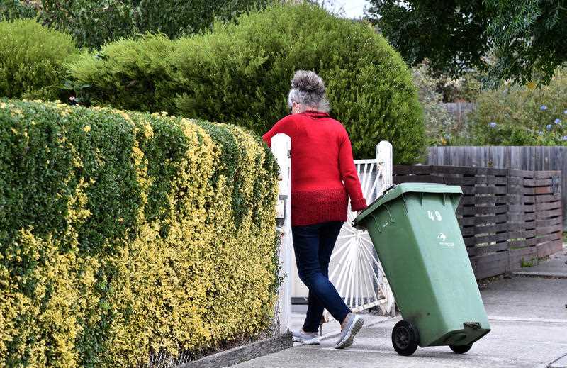 A woman takes in a household wheelie bin