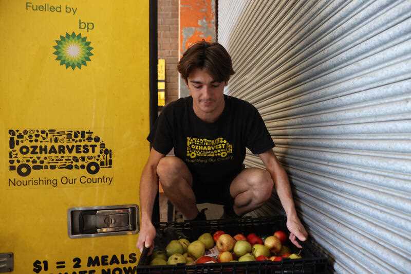 OzHarvest driver Sage Mcateer sorting through donated food at the back of a Woolworths supermarket dock