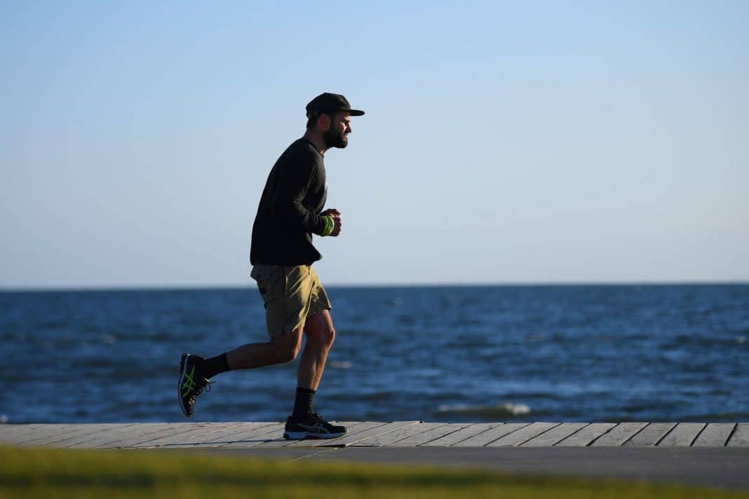 A man in his 30s is seen running along a boardwalk by the sea