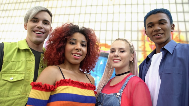 group of multiracial teenagers in colourful clothes smiling at the camera