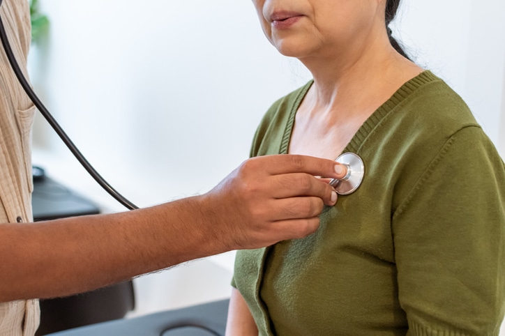 Close up shot of doctor using a stethoscope to check a mature adult woman's heart.