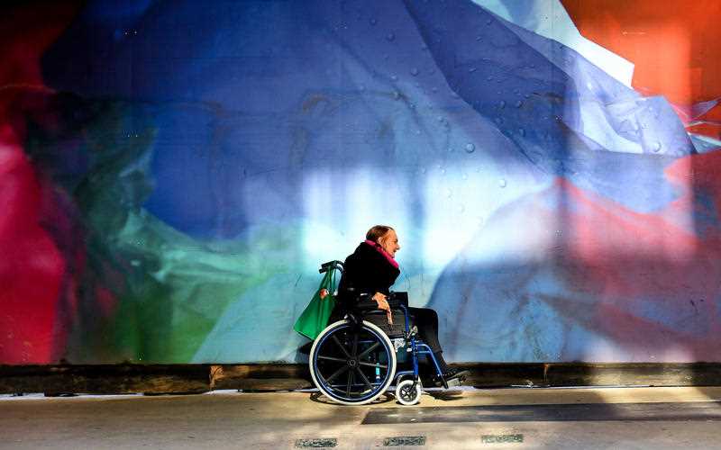 A wheelchair bound pedestrian is seen on a city footpath