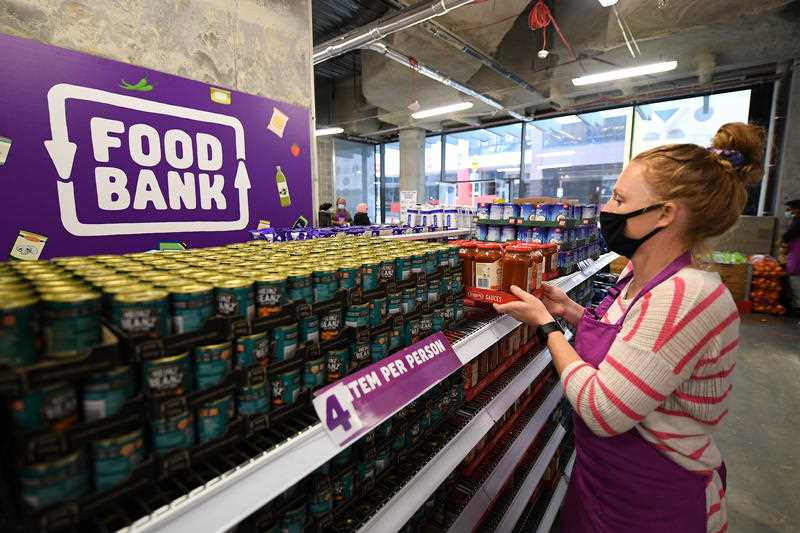 a Foodbank worker is seen stacking shelves with non perishable food items