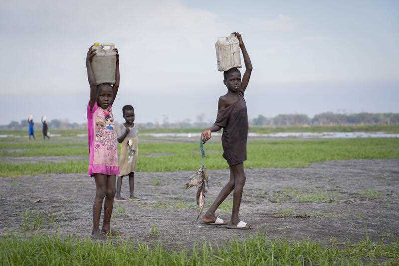 3 Children carry water on their heads and fish that they caught from a swamp in Canal-Pigi county, South Sudan Thursday, May 4, 2023