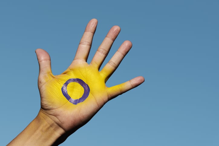 closeup of the intersex flag painted in the palm of the hand of a young person, against the blue sky