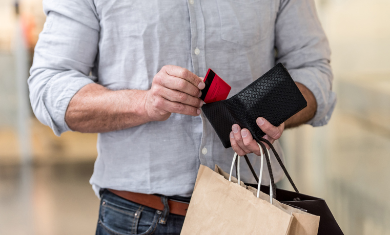 Unrecognizable shopping man putting credit card in his wallet while walking at the mall.